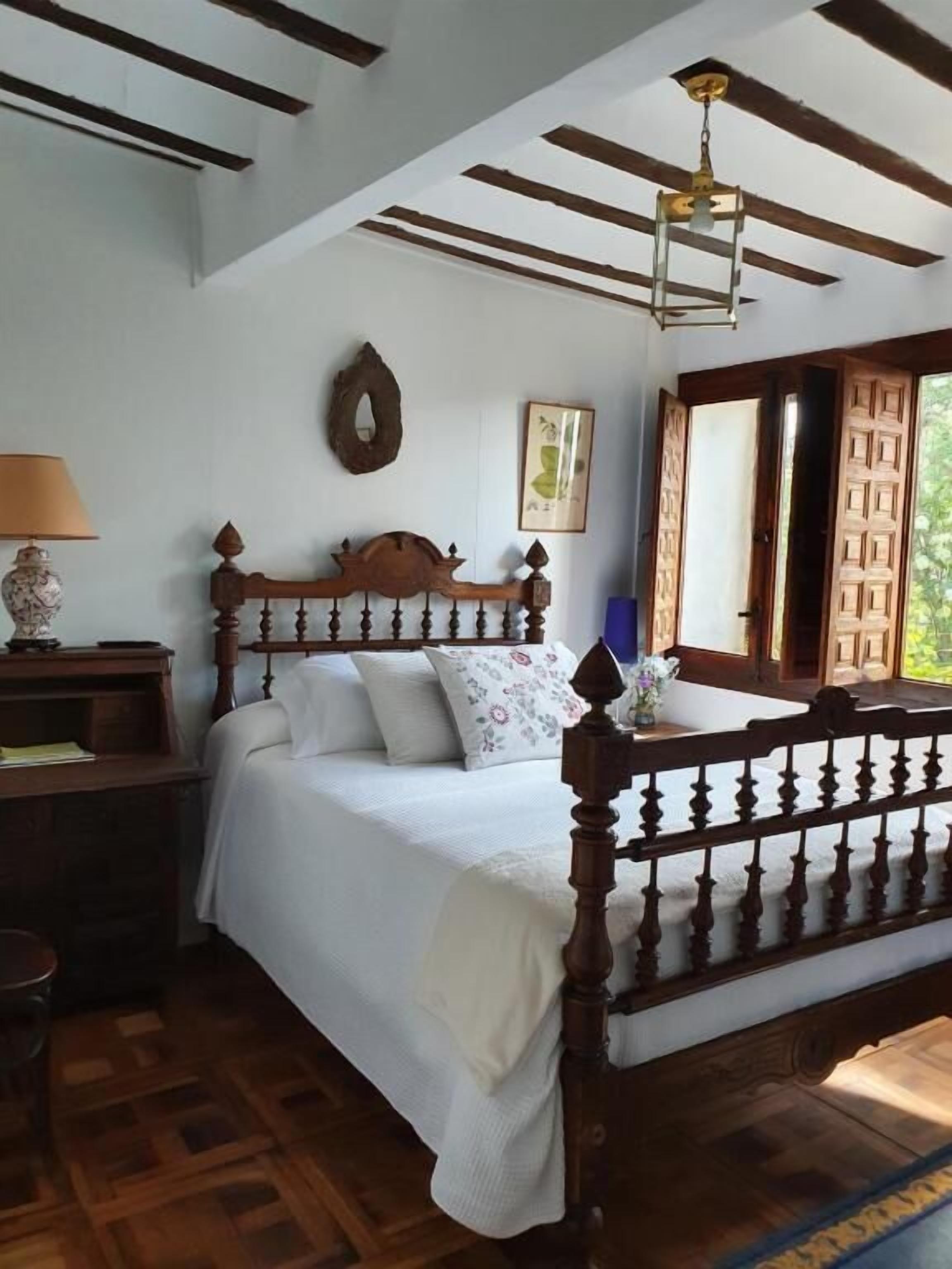 A bedroom with a wooden bed, a nightstand, a lamp, a wall-mounted mirror, and a ceiling fan.