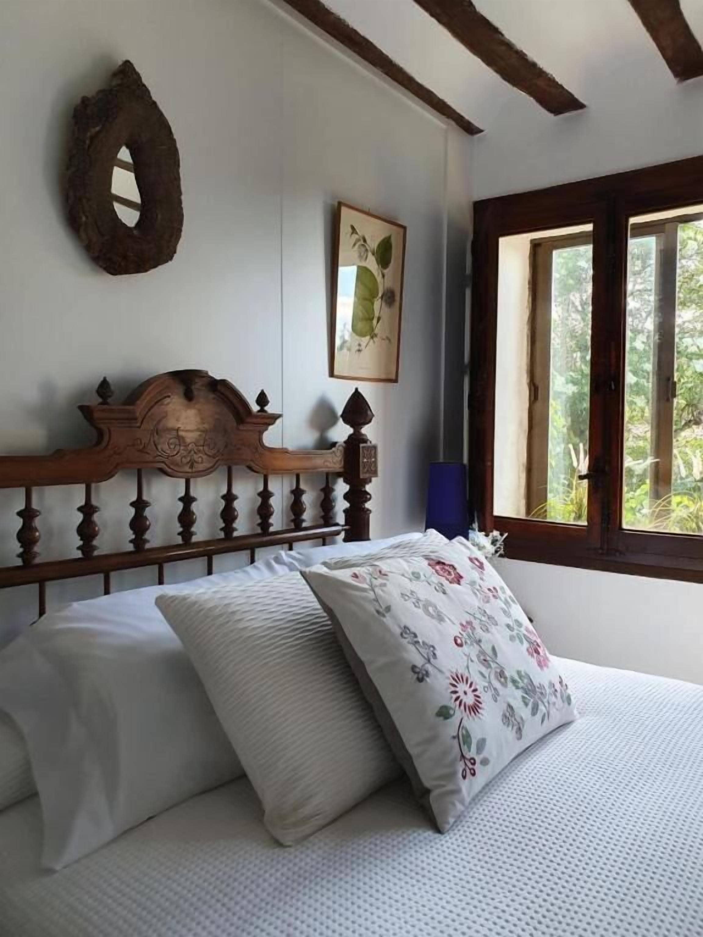 Un dormitorio con cabecera de madera, un grabado botánico enmarco y una ventana con vista a zonas verdes.