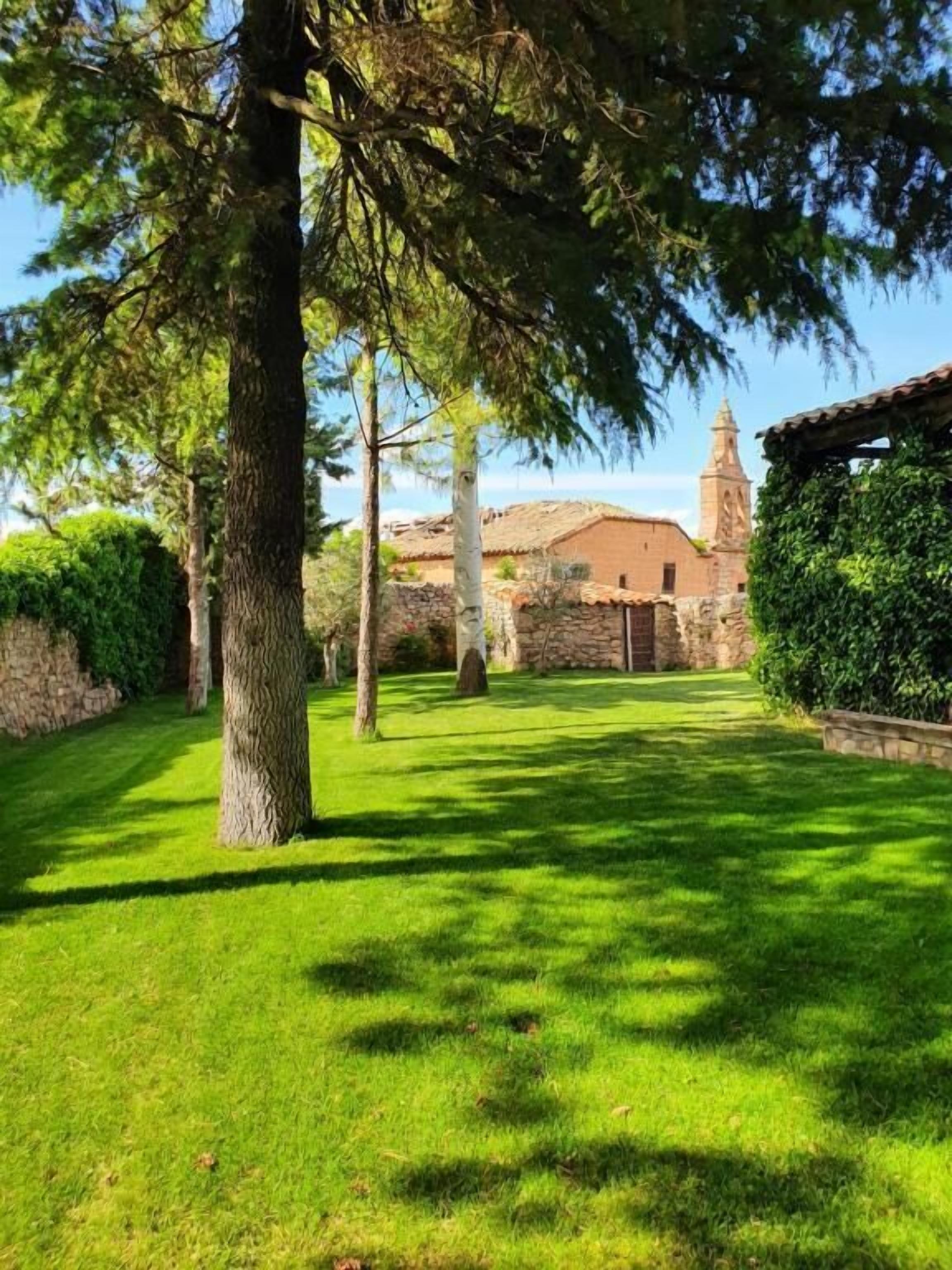 A well-maintained grassy courtyard with stone walls and a building with a bell tower in the background.