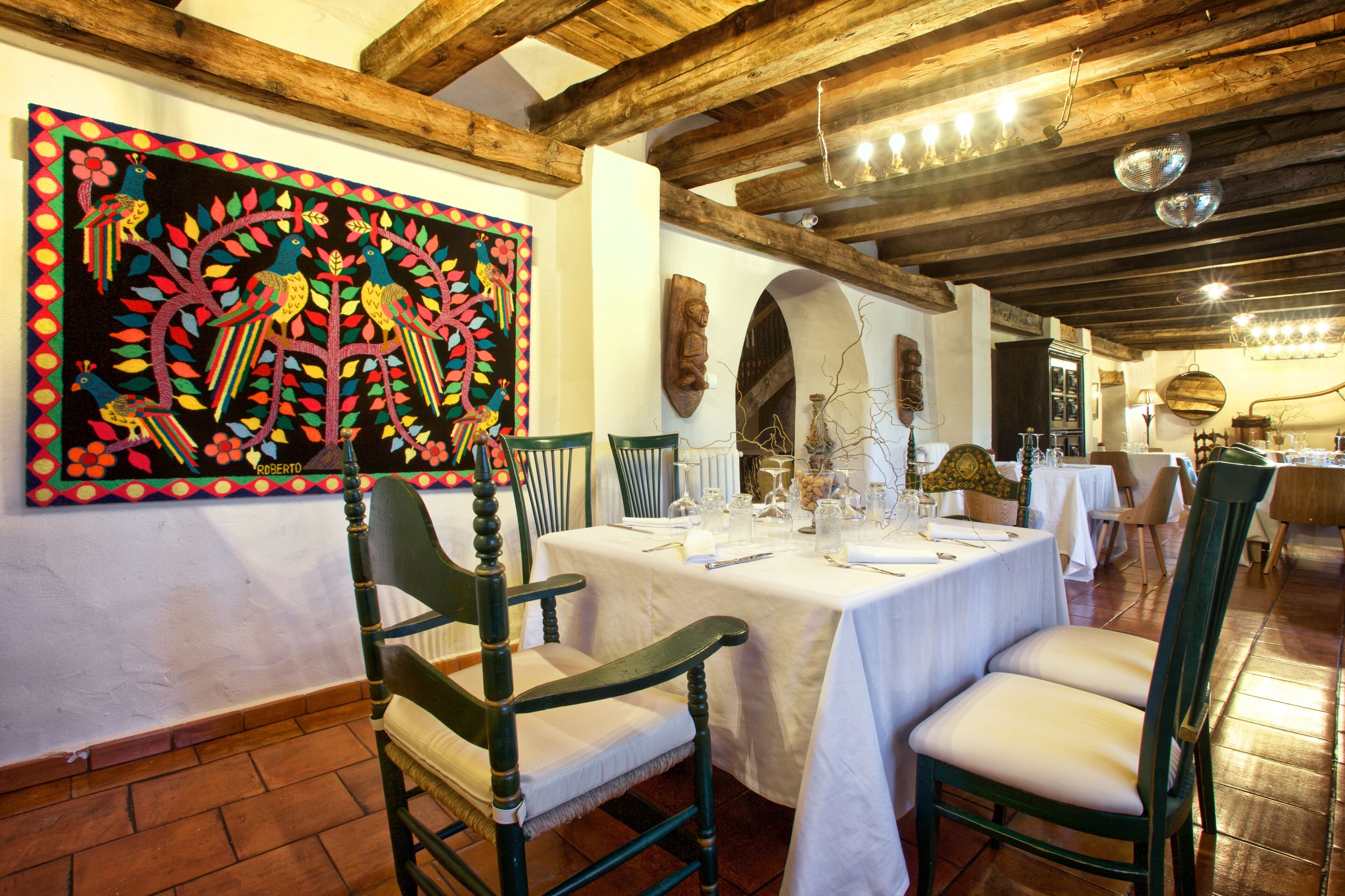 Un comedor con vigas de madera, un mural y una mesa dispuesta para una comida.