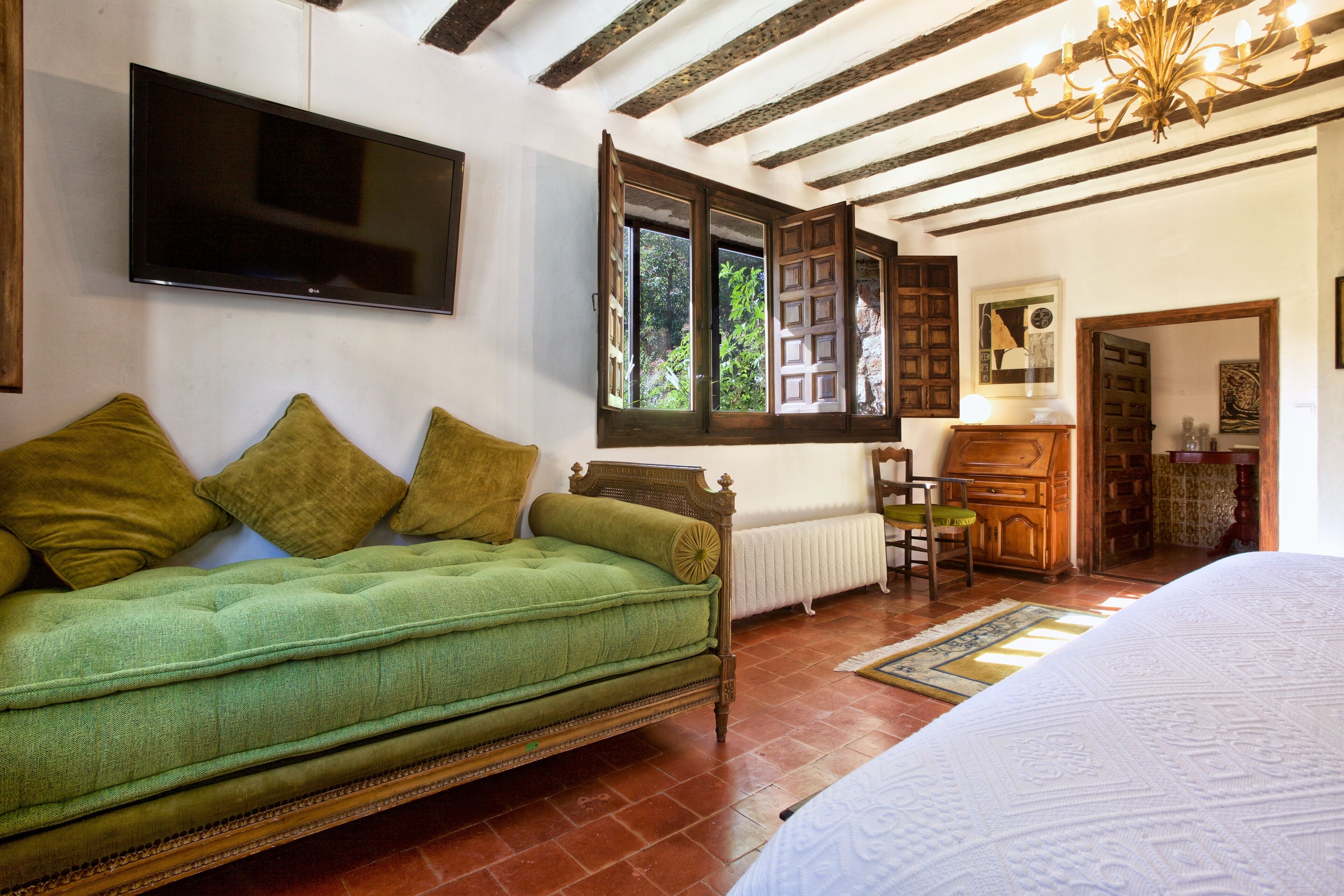 Una habitación con sofá verde, cama, televisor montado en la pared y aparador de madera.