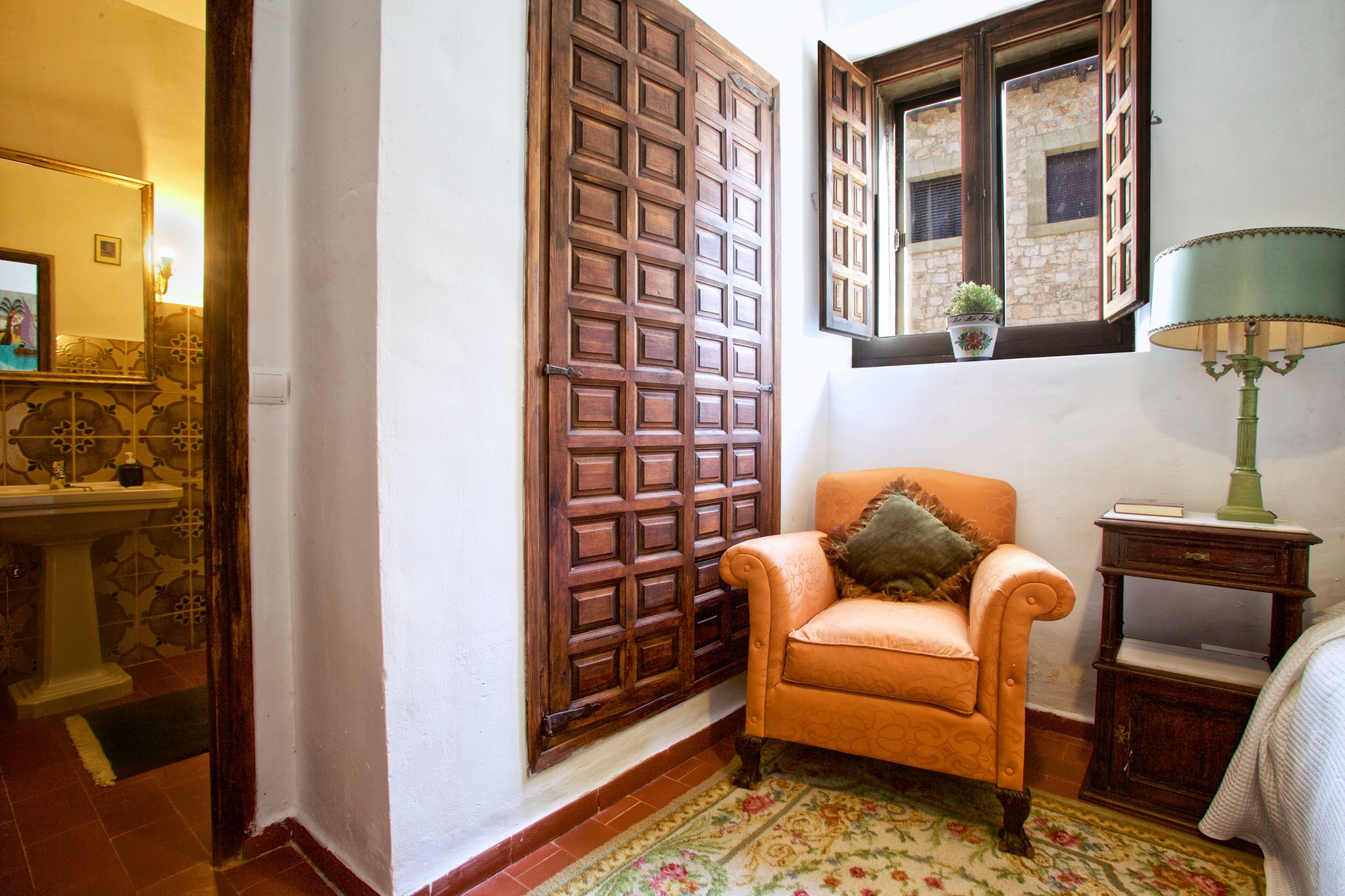 Una habitación con una puerta de madera, una silla, una lámpara y una pequeña mesa.