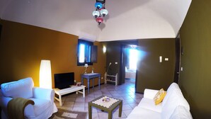 Ein Wohnzimmer mit einem weißen Sofa, einem kleinen Couchtisch, einem Fernseher und einem Fenster mit Jalousien.