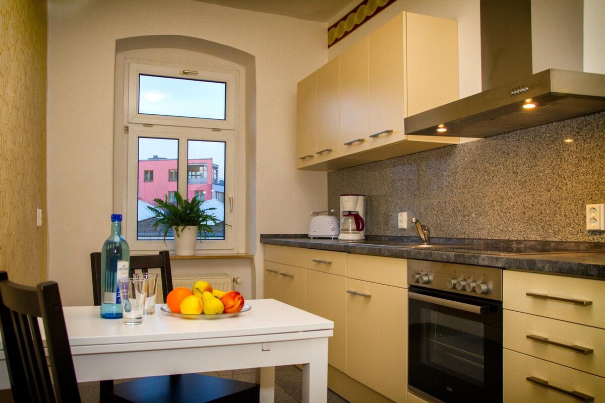 Una cocina compacta con ventana, una mesa con frutas, una cafetera y una estufa.