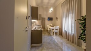 Een moderne keuken met een ingebouwde kookplaat, een eethoek met een witte tafel en stoelen, en een groot raam met gordijnen.