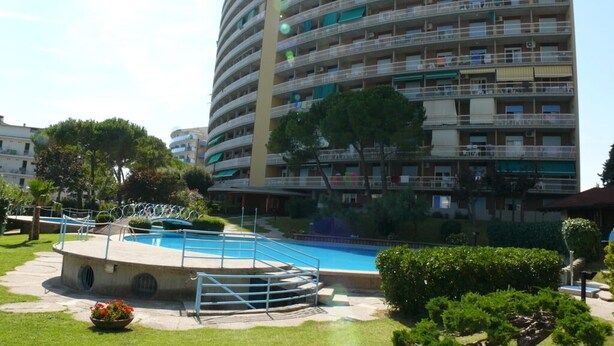 Un edificio residencial de varios pisos con balcones, piscina y zonas verdes circundantes.