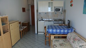 Cocina compacta equipada con microondas, estufa y lavaplatos. Hay una mesa de comedor con sillas y un sofá.