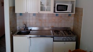 Una cocina compacta con gabinetes blancos, un microondas, una estufa a gas y un lavamanos.