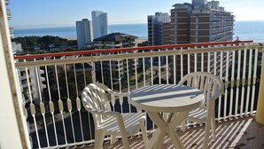 Un balcón con una mesa y dos sillas, con vistas a un paisaje urbano que incluye edificios y una playa.
