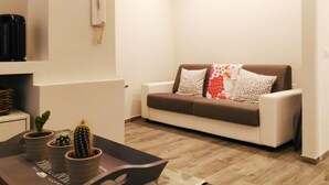 Een woonkamer met een bank, twee decoratieve kussens, een bijzettafel met potplanten en een aan de muur bevestigde telefoon.
