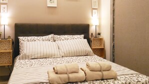Een netjes opgemaakt bed met gestreept bedlinnen, twee bedlampen en een kleine plant op het nachtkastje.