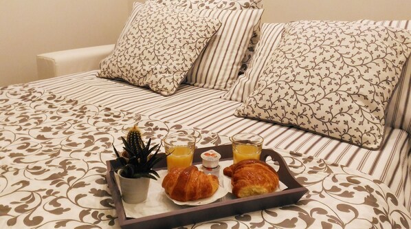 A neatly made breakfast tray with croissants, orange juice, and a cactus plant on a bed with patterned bedding and pillows.