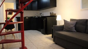 Een moderne keuken met donkere kasten, een rode spiraaltrap, een eethoek met een tafel en stoelen, en een woonkamer met een bank en kussens.