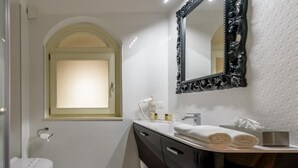 Une salle de bain avec des toilettes blanches, un lavabo avec un meuble noir, un miroir doté d’un cadre orné et une fenêtre avec un cadre blanc.