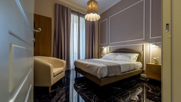 Une chambre d’hôtel moderne avec un grand lit, un coin salon avec un fauteuil et un sol en marbre.