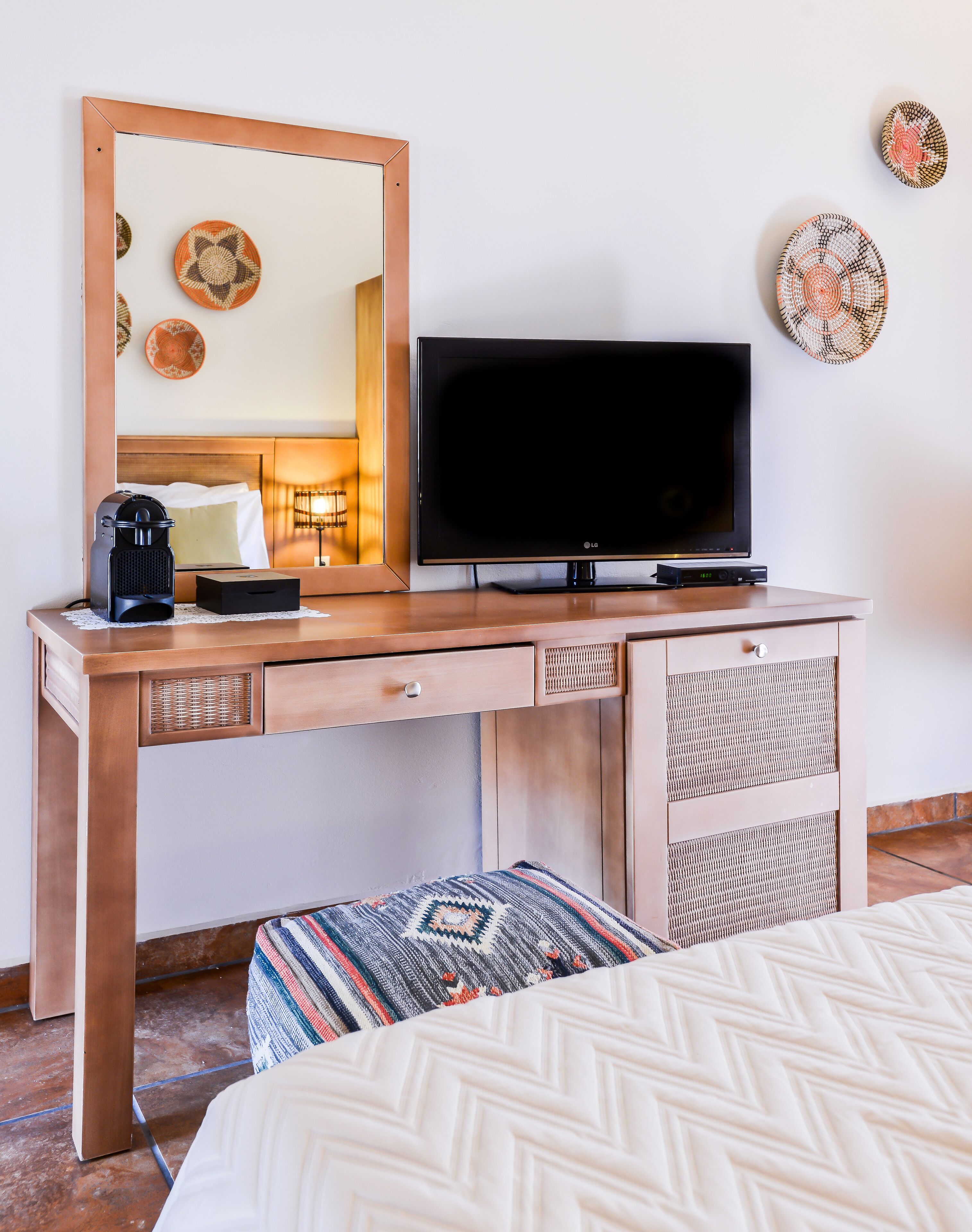 A hotel room with a wooden desk, a flat-screen TV, a coffee maker, and a bed with patterned bedding.