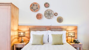 Een keurig opgeruimde hotelkamer met een groot bed, twee nachtkastjes, een telefoon aan de muur en decoratieve wandkunst.