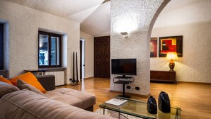 A living room with a beige sofa, a glass coffee table, a flat-screen TV, and a lamp. - Art Apartment with lake-view terrace, parking, and turkish bath. (Cernobbio)