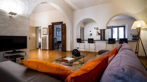 A living room with a flat-screen TV, a sofa with orange cushions, a coffee table, and a lamp. - Art Apartment with lake-view terrace, parking, and turkish bath. (Cernobbio)