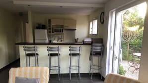 Cocina compacta con microondas, refrigerador y taburetes de bar. Se ve vegetación a través de la ventana.