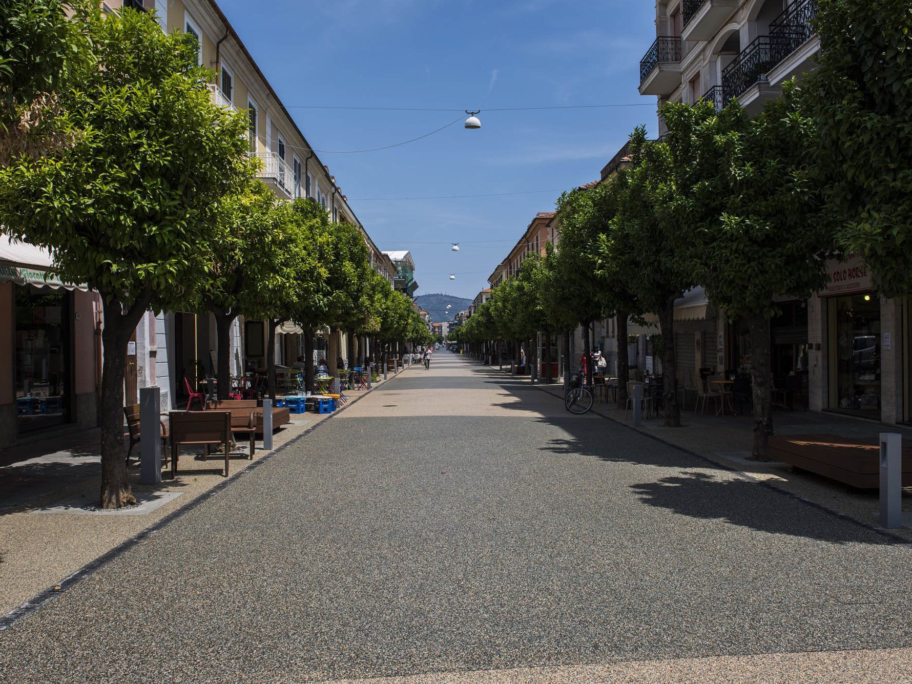 A tree-lined street with buildings on either side, benches, and outdoor seating.