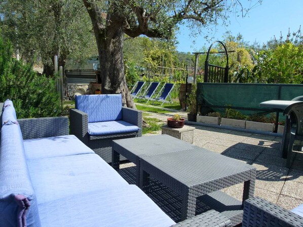 A patio with wicker furniture, including a sofa and two chairs, a small table, and a green garden bed in the background.