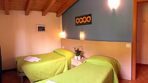 A room with two beds, a nightstand with a lamp and flowers, and a wall-mounted light fixture. - Lake Como - Residence La Collina - Strawberry (Vercana)