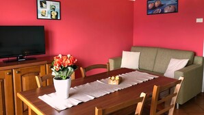 A dining area with a wooden table, chairs, a television, a red wall, and a painting. - Lake Como - Residence La Collina - Strawberry (Vercana)