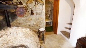 Una habitación rústica con una gran rueda de piedra, una mesa de madera con una silla y una escalera que lleva a una puerta.