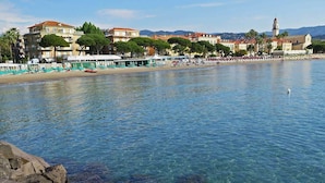 Un pueblo costero con aguas cristalinas, un litoral rocoso y edificios al fondo.