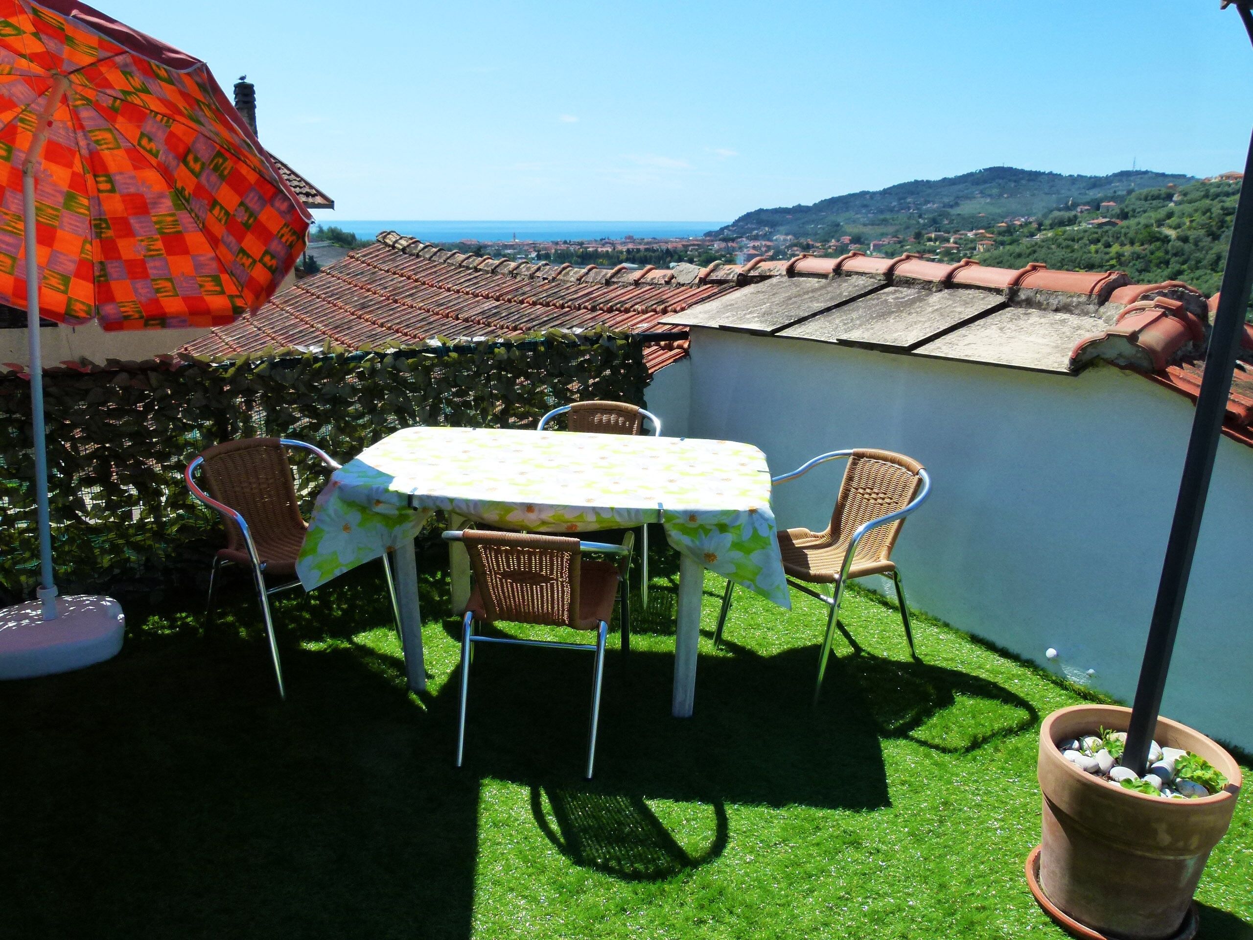 A patio with a table and chairs, a potted plant, and a view of the sea and hills.