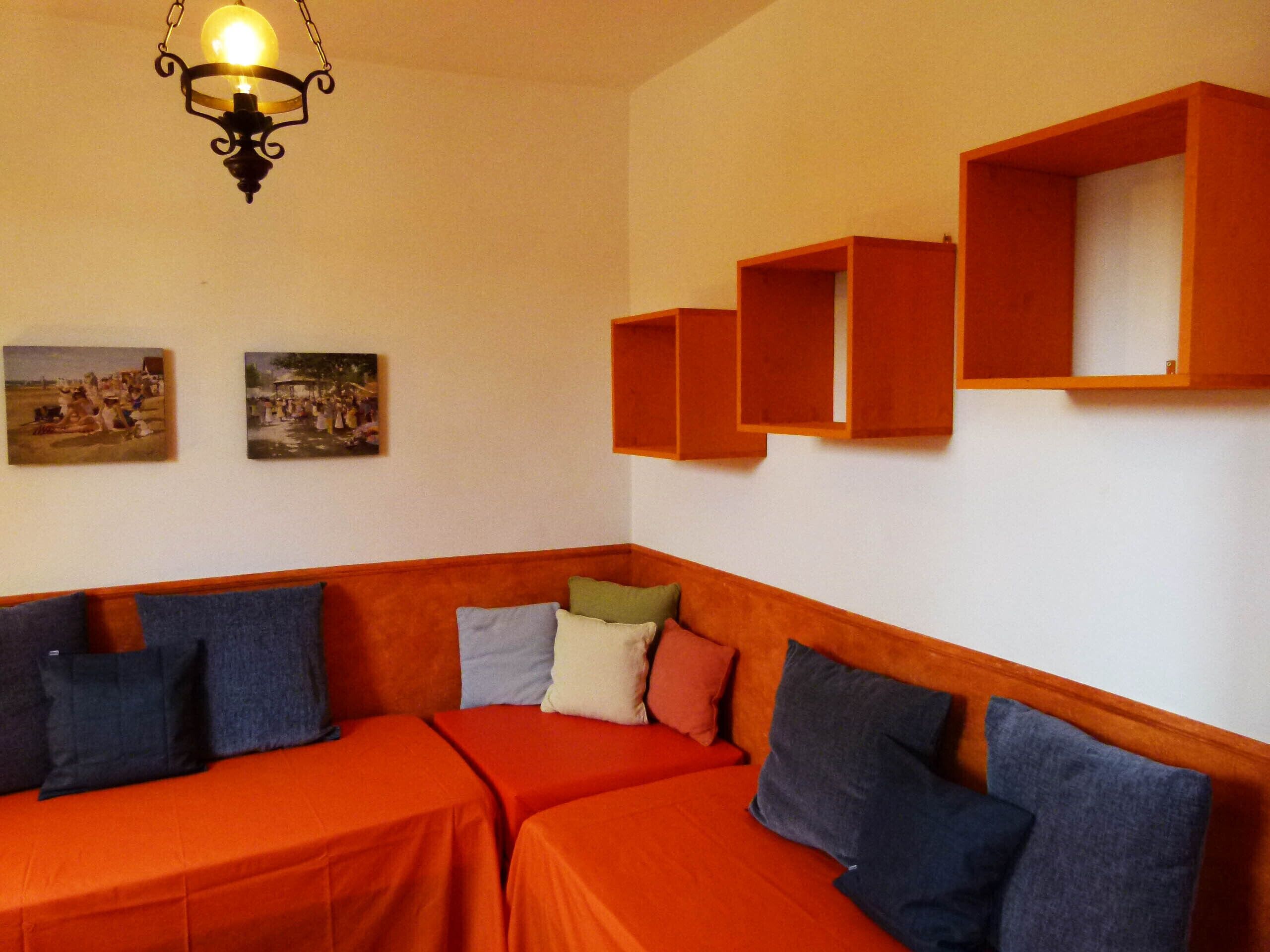 A room with two orange beds, a hanging light fixture, and wooden shelves above the beds.