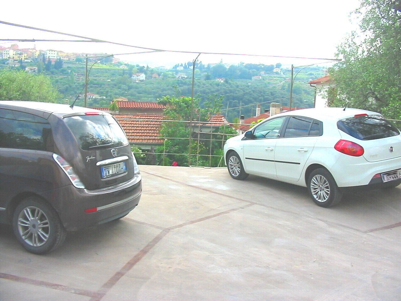 Two cars parked in a driveway with a view of a hilly landscape in the background.