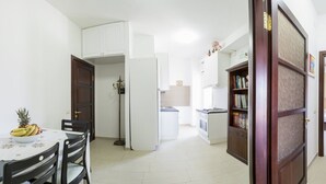 A kitchen with white cabinets, a dining table with chairs, a refrigerator, a stove, and a bookshelf. - The terrace on the park - bathrooms in the room - panoramic - near the beach (Quartu Sant'Elena)
