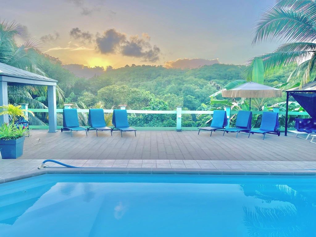 Un espace piscine agrémenté de chaises longues et de parasols, entouré d’une végétation luxuriante et offrant une vue sur un paysage montagneux.