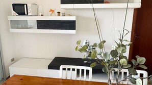Un comedor con una mesa de madera, sillas blancas, un florero con hojas verdes y un banco blanco.