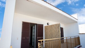 Un edificio moderno con fachada blanca, barandilla de balcón de madera y dos puertas con contraventanas.