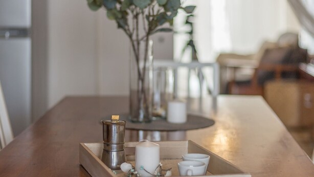 Una mesa de madera con una bandeja que contiene una cafetera de plata, una vela blanca y pequeños adornos.