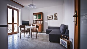 A modern living room with a dining area, a grey sofa, a TV, and a bookshelf.
