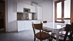 A modern kitchen with white cabinets, a stainless steel microwave, and a dining area with a glass table and wooden chairs.