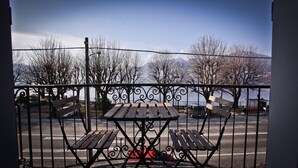 A balcony with a view of a lake and mountains, featuring two wooden benches and a metal railing.