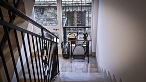 A staircase with a black railing, a stone wall, and a window with a metal grill.