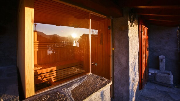 A wooden cabin with a large window, a stone wall, and a stone bench.