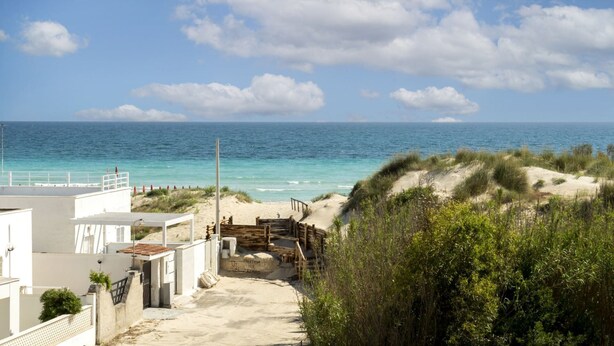 Ein Küstenblick mit Sandstrand, Holzzaun und einem weißen Gebäude mit Vordach.