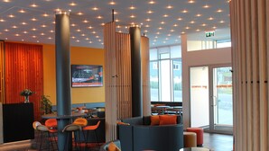 A modern hotel lobby with a seating area, a large pillar, and a television screen displaying a hotel advertisement. - HHE Express Hotel (Nuuk)