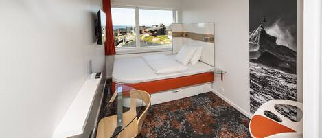 Una habitación de hotel moderna con cama, escritorio, silla, ventana grande y un mural en la pared.