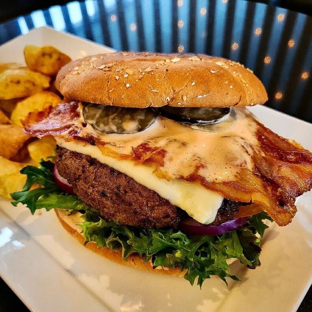 A burger with bacon, cheese, and lettuce on a bun, accompanied by fries.