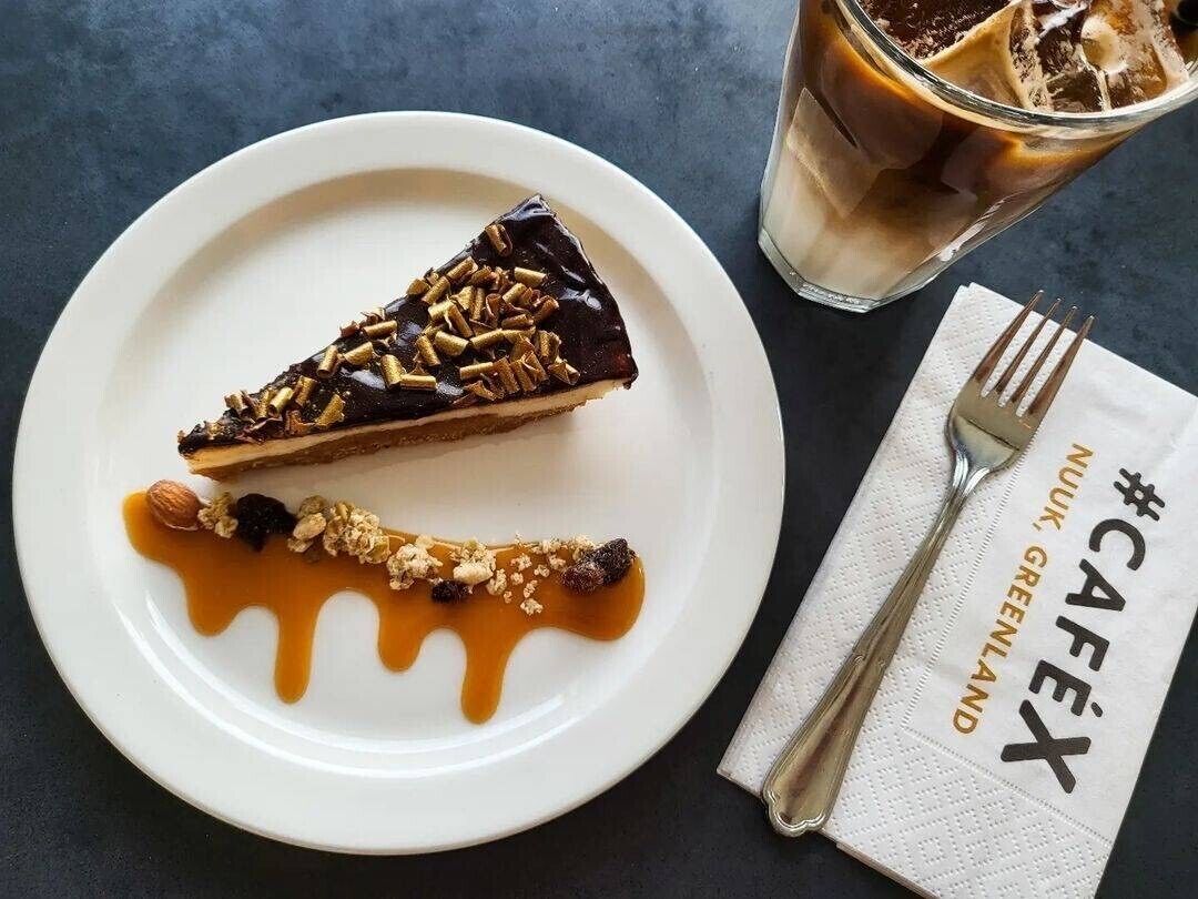 A dessert plate with a slice of pie topped with chocolate and nuts, a caramel sauce, and a glass of iced coffee.