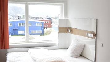 A modern hotel room with a glass bed, a small table, and a view of buildings outside.