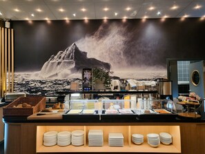 A buffet area with a mountain-themed mural, a fruit bar, and neatly stacked plates. - HHE Express Hotel (Nuuk)